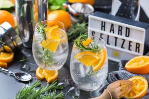 Hard seltzer cocktail with orange, rosemary and ice on a table. Summer refreshing beverage, drink on a black table