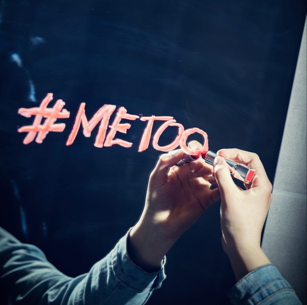 Girl writing "#metoo" on a mirror with a red lipstick.