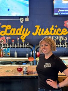 Frances standing with an Athletic Brewing Beer in the Lady Justice taproom.
